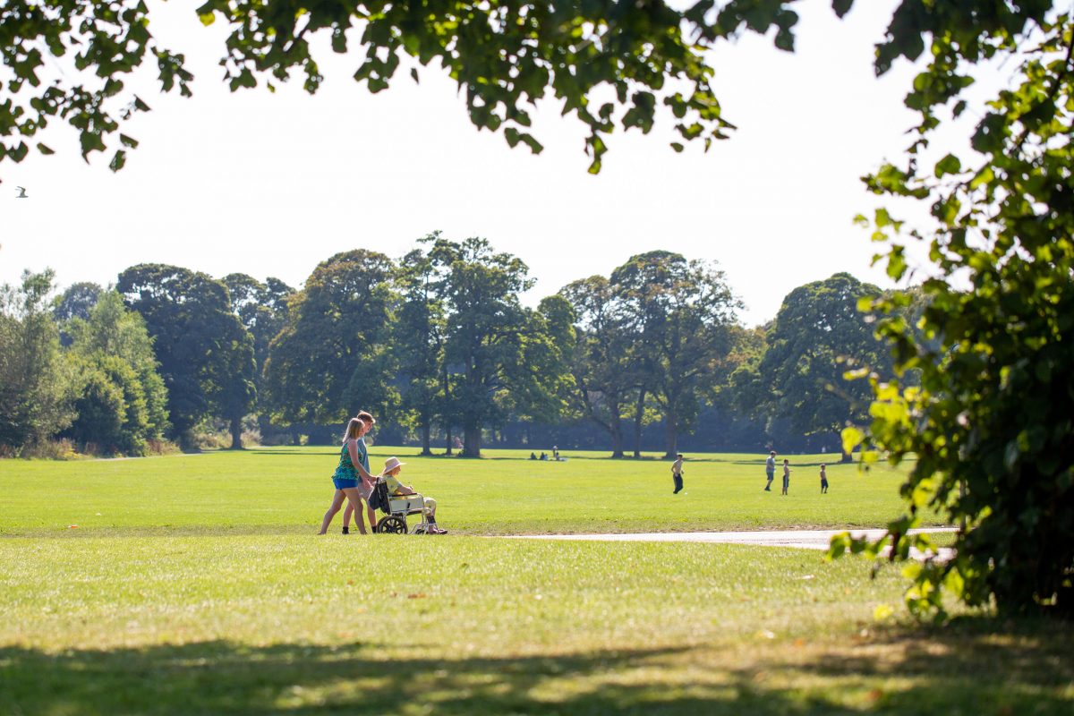 Woman and man walking in a park, pushing a lady in a wheelchair.
