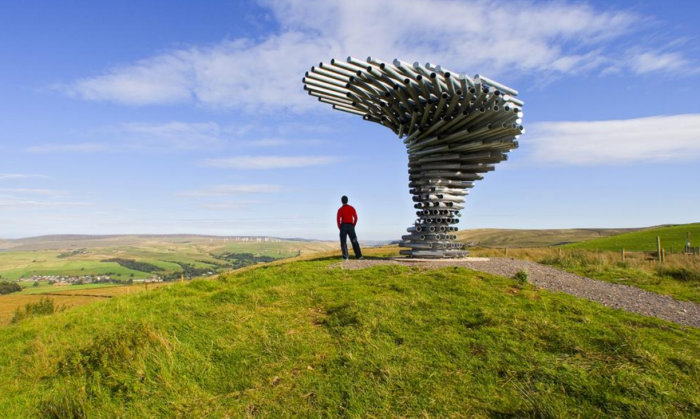 Lone person stood on hill, under singing ringing tree art installation.