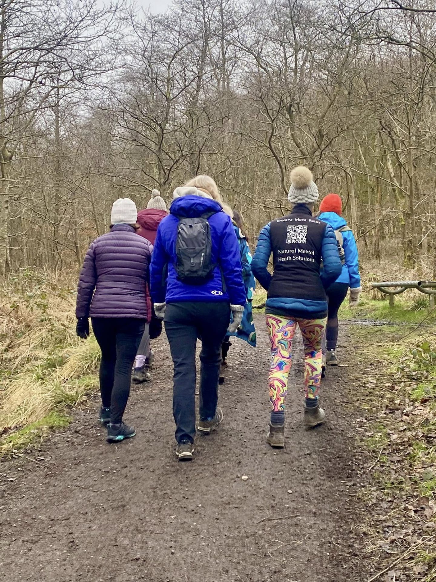 Group of ladies walking away from the camera on a muddy trail path through woodland